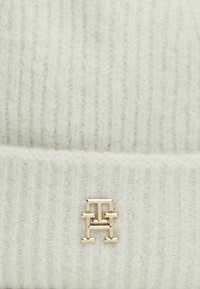 Berretto lavorato a maglia di colore grigio chiaro con una texture a costine e un leggero luccichio. Presenta un accento logo in tono oro sulla parte frontale per un tocco di dettaglio in più.