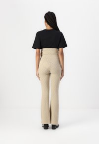 Høytlivete beige bukser med diamantmønster og utsvingte ben, kombinert med en svart T-skjorte med korte ermer. Glatt tekstur, minimalistisk design.