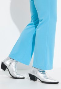 Bottines en silver métallique avec un bout pointu, un talon bloc et une finition texturée, associées à un pantalon large bleu clair.