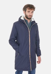 Parka con cappuccio blu navy con zip frontale, rivestimento in pelliccia e accenti a righe. Presenta maniche lunghe e tasche laterali, realizzata in un materiale leggero.