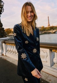 Blazer cruzado de terciopelo azul marino adornado con detalles de estrella y destello solar con acentos dorados, con un acabado texturizado y un corte entallado.