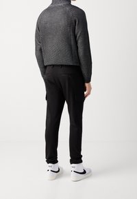 Černý žebrovaný svetr s vysokým límcem, kratšího střihu, kombinovaný s černými cargo kalhotami s bočními kapsami a bílými teniskami.