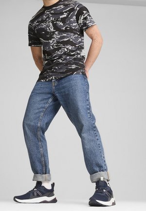 Černé a šedé maskovací tričko, modré džíny, ohrnuté manžety a námořnické tenisky s bílými akcenty. Volný střih, moderní vzory.