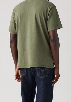 Olive green cotton t-shirt with short sleeves, crew neck, and straight hem, paired with dark blue denim jeans. Back view shows smooth texture.