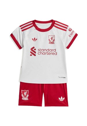 Dziecięcy strój piłkarski Liverpool Football Club z białą koszulką z czerwonymi paskami, logo oraz czerwonymi spodenkami z logo klubu i marki.