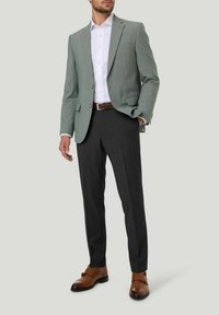 Hellgrüner kariert Blazer über einem weißen Hemd, kombiniert mit dunkelgrauen Hosen und braunen Anzugschuhen. Einfaches Design und maßgeschneiderte Passform.
