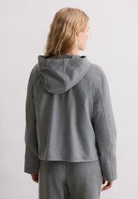 Szara kurtka z kapturem o luźnym kroju, charakteryzująca się miękką fakturą i kapturem na sznurek, pokazana od tyłu, z długimi rękawami i minimalną ilością szwów.