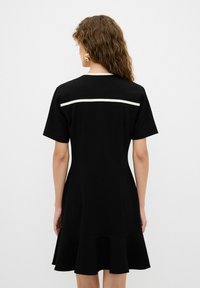 Vestido negro de manga corta en tela suave con dobladillo acampanado, que presenta una franja horizontal blanca en la parte superior de la espalda.