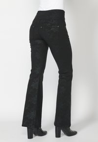 Vaqueros negros acampanados con un patrón floral texturizado, que presentan una cintura alta, bolsillos traseros y acentos decorativos de hardware plateado.