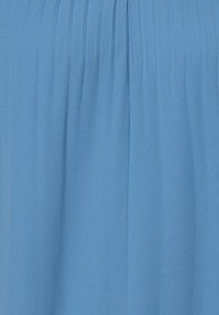 Blauwe stof met een zachte textuur, voorzien van subtiele plooien die verticaal door het midden lopen, wat een vloeiende uitstraling creëert.