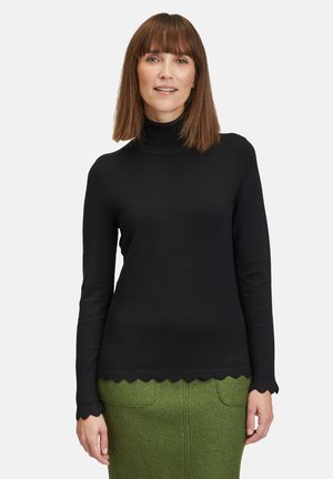 Schwarzer Rollkragenpullover mit langen Ärmeln und gewelltem Saumdetail, hergestellt aus einem glatten Strickstoff, kombiniert mit einem grünen strukturierten Rock.