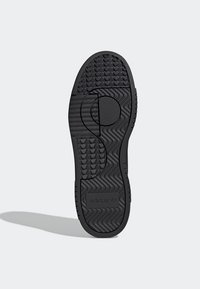 Suola di sneaker nera in gomma con motivi testurizzati e scanalature, caratterizzata da un dettaglio circolare e dal logo "adidas" impresso sul tallone.