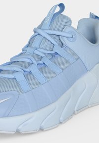 Ανοιχτό μπλε αθλητικό παπούτσι Nike Free με επάνω μέρος από δίχτυ, επικαλύψεις με λουράκια, μαλακή σόλα και θηλιά έλξης στη μαξιλαρωμένη γλώσσα.