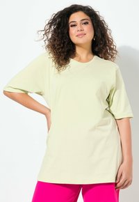 T-shirt oversize verde chiaro con maniche corte, realizzata in tessuto morbido. Abbinata a pantaloni rosa brillante, con scollatura rotonda e vestibilità comoda.
