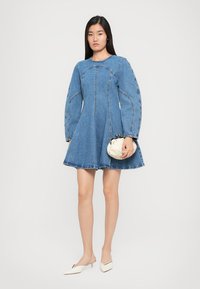 Denimová áčková šaty s dlhými balónovými rukávmi, surovým okrajom a viditeľnými švami. Skombinované s malou béžovou kabelkou a mules.