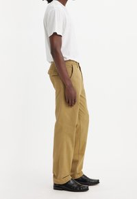 Lätta khaki-byxor med rak passform, märkbara sömdetaljer och bakfickor, tillsammans med svarta läderskor.