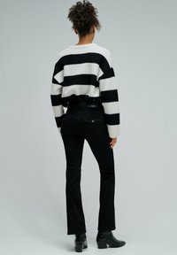 Suéter a rayas negro y blanco con un corte holgado, combinado con jeans negros y botines. Enfoque en la textura y los colores contrastantes.