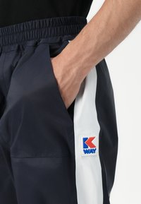 Marineblå shorts med hvit sidepanel, elastisk midje og synlig K-WAY-logo på lommen. Glatt og lett stofftektur.