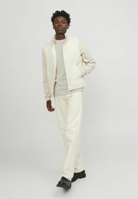 Light-colored, zip-up jacket made of smooth fabric with a structured design, paired with matching pants and black boots for contrast.