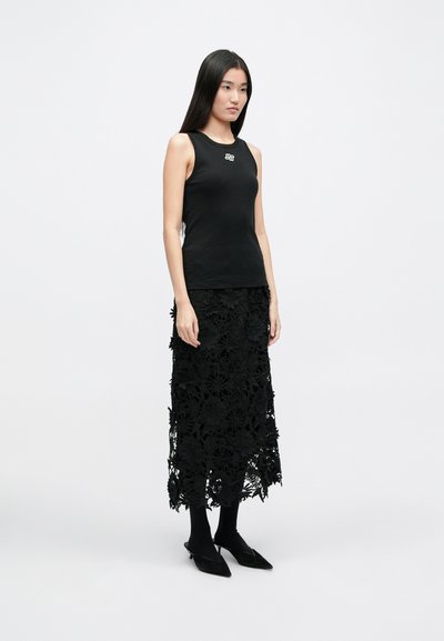 Μαύρο ριγέ αμάνικο μπλουζάκι με λευκό λογότυπο, σε συνδυασμό με μια μακριά μαύρη δαντελένια φούστα με λουλουδάτες εκτυπώσεις και στρωματοποιημένο σχέδιο. Μαύρα παπούτσια και καλσόν.