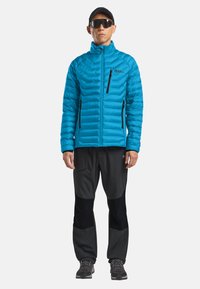 Giacca isolante blu con chiusura a zip e accenti neri, abbinata a pantaloni softshell neri con tasche con zip e sezioni rinforzate.