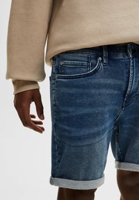 Shorts en denim bleu foncé avec un effet délavé. Caractéristiques : coupe standard, bords retournés et design à cinq poches.