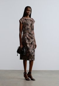 Õiekujundusega varrukateta kleit roosades ja pruunides toonides, liibuvaga lõige. Kaunistatud väikese musta kotiga ja mustade rihmikandadega kontsakingadega.