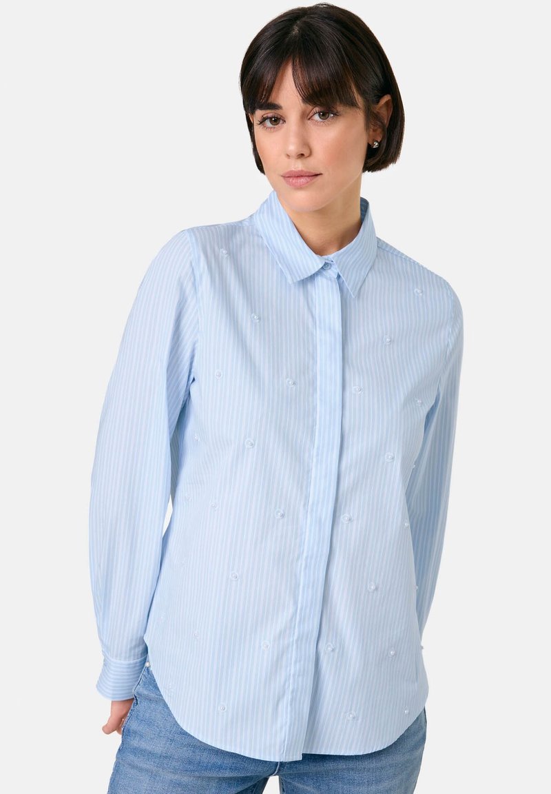 Light blue, long-sleeve shirt with white vertical stripes, button-up front, and embroidered embellishments on the fabric. Rounded hem.