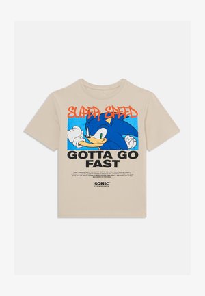 Camiseta de algodón color beige con gráfico de Sonic el Erizo, "SUPER VELOCIDAD" en rojo, "DEBO IR RÁPIDO" en negrita negra abajo, sobre un fondo azul vibrante.