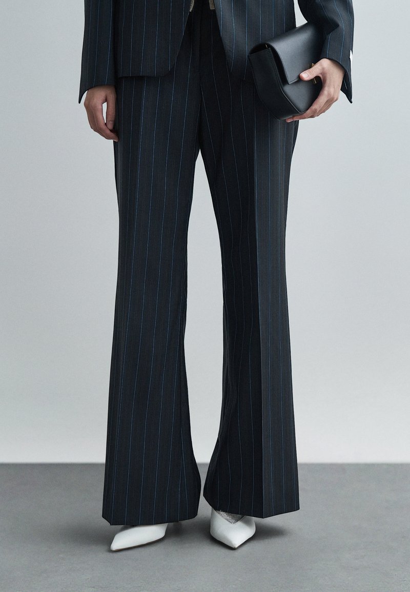 Navy sinised triibulised püksid flared kujuga, valmistatud siledast kangast. Kombineeritud valgete teravate ninadega kontsakingade ja väikese musta käekotiga.