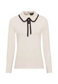 Krämfärgad långärmad topp med svart kantad Peter Pan-krage och svart sidentie vid halslinjen.