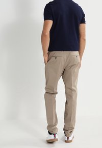 Chino beige realizzati in cotone, con vestibilità slim, due tasche posteriori con bottoni e una texture liscia, abbinati a sneakers bianche.