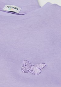 Camiseta para niños de color lavanda con una pequeña mariposa bordada en el pecho y una etiqueta de la marca Tezenis Kids dentro del cuello.