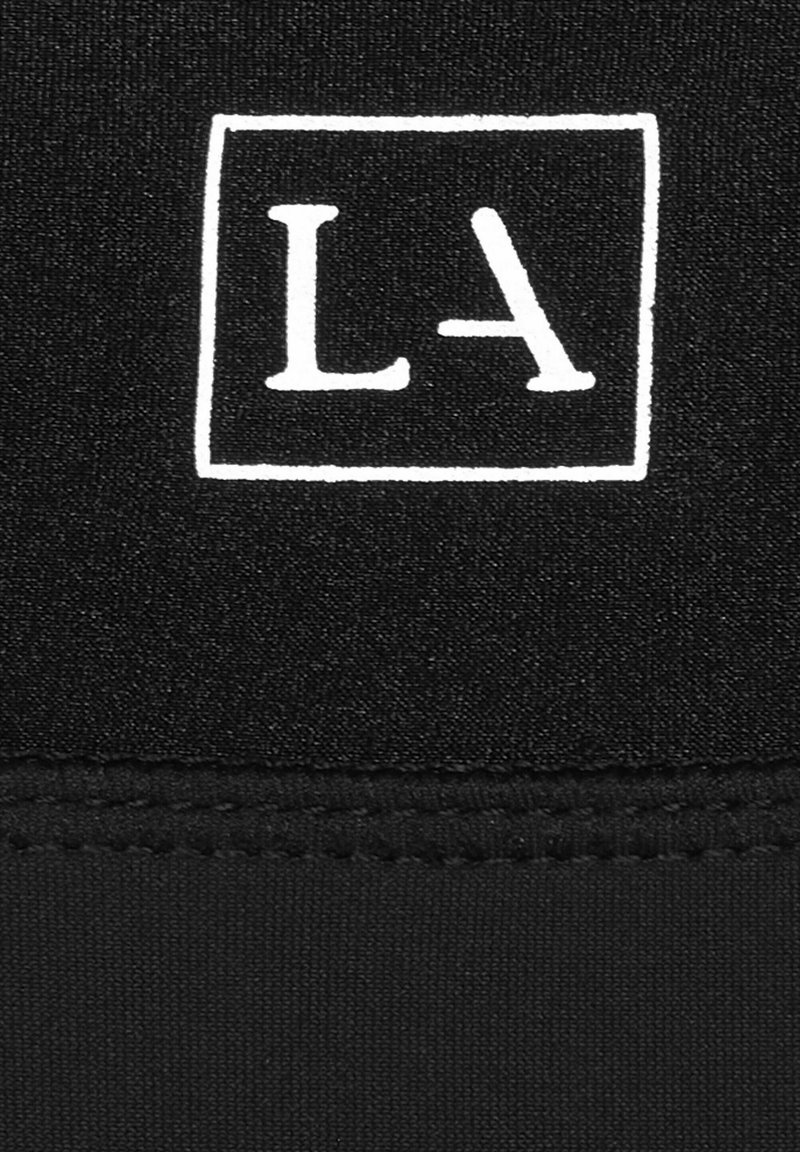 Schwarzer Stoff mit glatter Textur, auf dem ein weißes rechteckiges Logo mit den Buchstaben "LA" abgebildet ist. Die Nähte sind an den Kanten sichtbar.