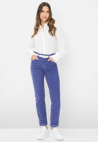 Camicia bianca con bottoni, pantaloni in corduroy blu con risvolti, cintura bianca e sneakers bianche. Tessuto liscio e vestibilità su misura.