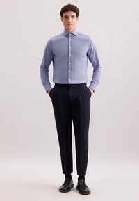 Lichtblauw overhemd met lange mouwen en een knoopsluiting aan de kraag, gecombineerd met donker, op maat gemaakte broek en zwarte leren schoenen.