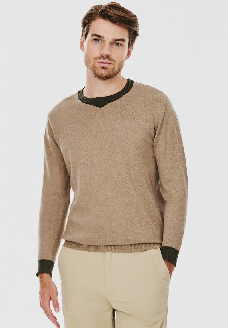 Beżowy sweter wykonany z miękkiego materiału, z dekoltem w kształcie litery V oraz ciemnozielonym prążkowanym kołnierzykiem i mankietami. Długie rękawy i dopasowany krój.