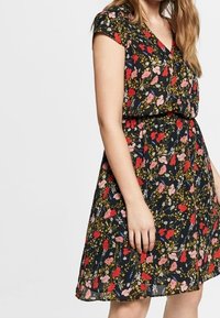 Květinové šaty z černé látky s červenými a růžovými květy a zelenými listy. Mají krátké rukávy, výstřih do V a vytažený pas.