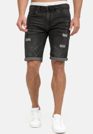 Shorts in denim scuro con risvolti, caratterizzati da macchie usurate sul davanti. Indossati con sneakers bianche e una cintura elastica.