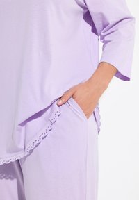 Ropa de estar por casa en color lavanda con un corte relajado, tejido suave y un borde festoneado cerca del bolsillo, con mangas de tres cuartos.