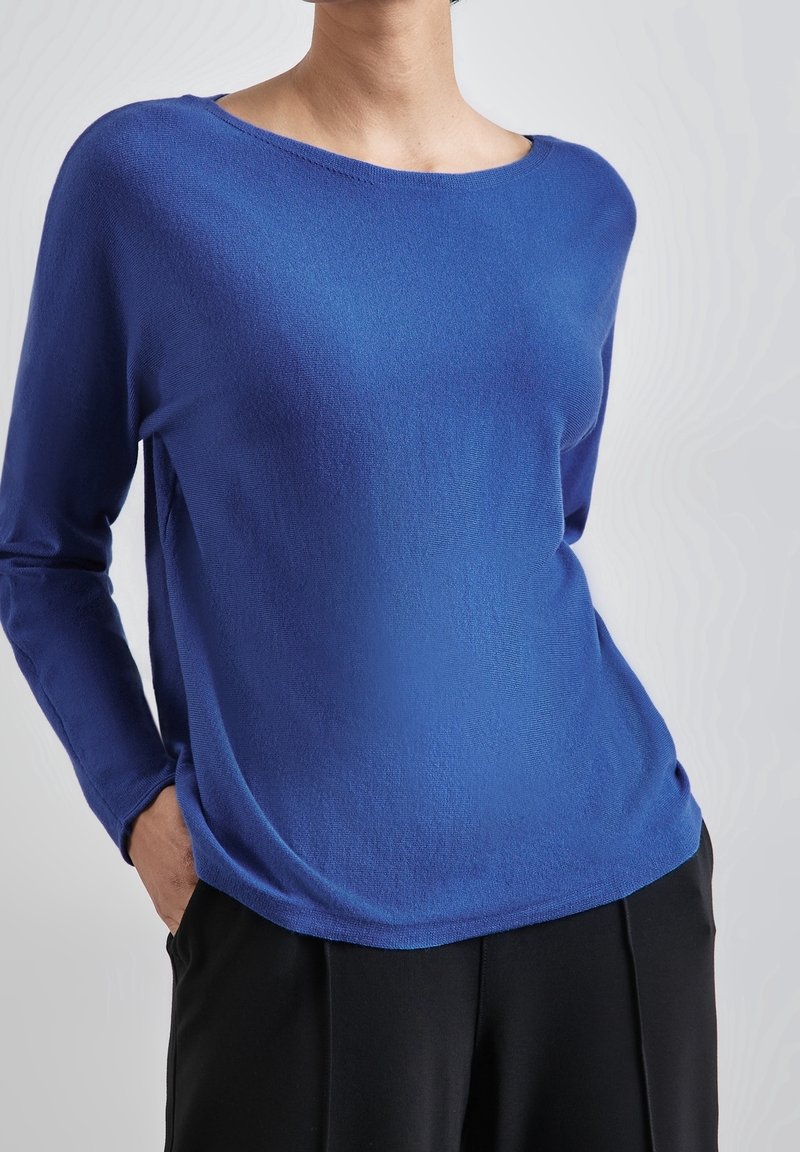 Blue knit long-sleeve top with a wide neckline, relaxed fit, and smooth texture, paired with black trousers. Simple design, no visible patterns.