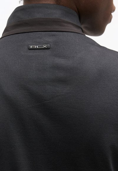 Μαύρο ένδυμα με γιακά και μεταλλικό λογότυπο «RLX» στο πάνω μέρος της πλάτης, φορεμένο από ένα άτομο που φαίνεται από πίσω και ελαφρώς από το πλάι.