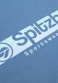 Blauer Baumwollstoff mit glatter Textur zeigt weißen fetten Text mit der Aufschrift "Spitzb" und "Sportswear", akzentuiert mit einem Logo.