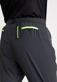 Grå atletiske shorts med snøre i taljen, grønne kontrastlynlåse og to sidelommer med kontrasterende grønne stikninger.