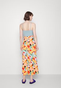 Vestido maxi floral com um padrão colorido, apresentando um corpete justo azul claro e uma saia fluída estampada. Combinado com sandálias azul escuro.