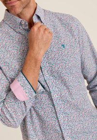 Overhemd met knopen en een bloemenpatroon in roze, groen en blauw. Kenmerkt zich door een contrasterende roze manchette en kraagafwerking, slim fit.