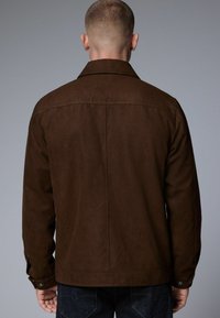 Brown suede jacket with a straight cut, long sleeves, and a pointed collar. Features button cuffs and a smooth texture.