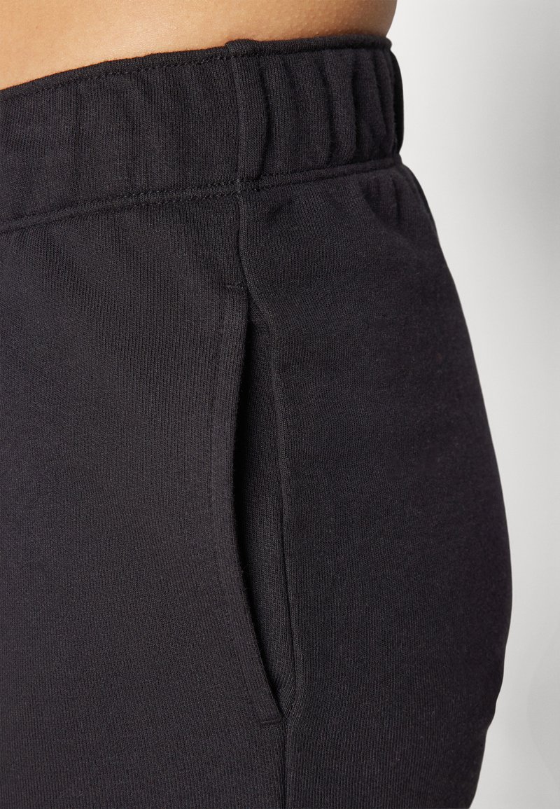 Pantaloni sportivi neri con vita elasticizzata, dotati di tasca laterale e tessuto liscio e texturizzato. Dettaglio ravvicinato della vita e della tasca.