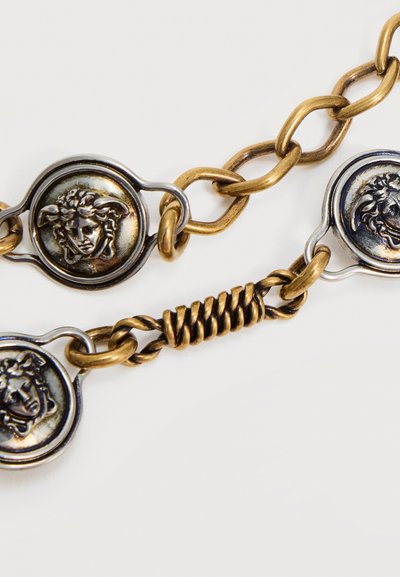Maillons de chaîne en or et argent avec trois médaillons ronds présentant des visages mythologiques classiques en relief sur un fond blanc.