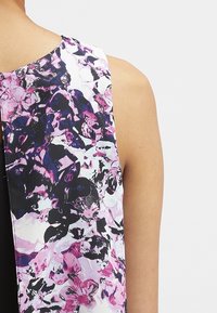 Top bez rukávů s barevným abstraktním květinovým vzorem v odstínech fialové, černé a bílé, s hladkou texturou a kulatým výstřihem.